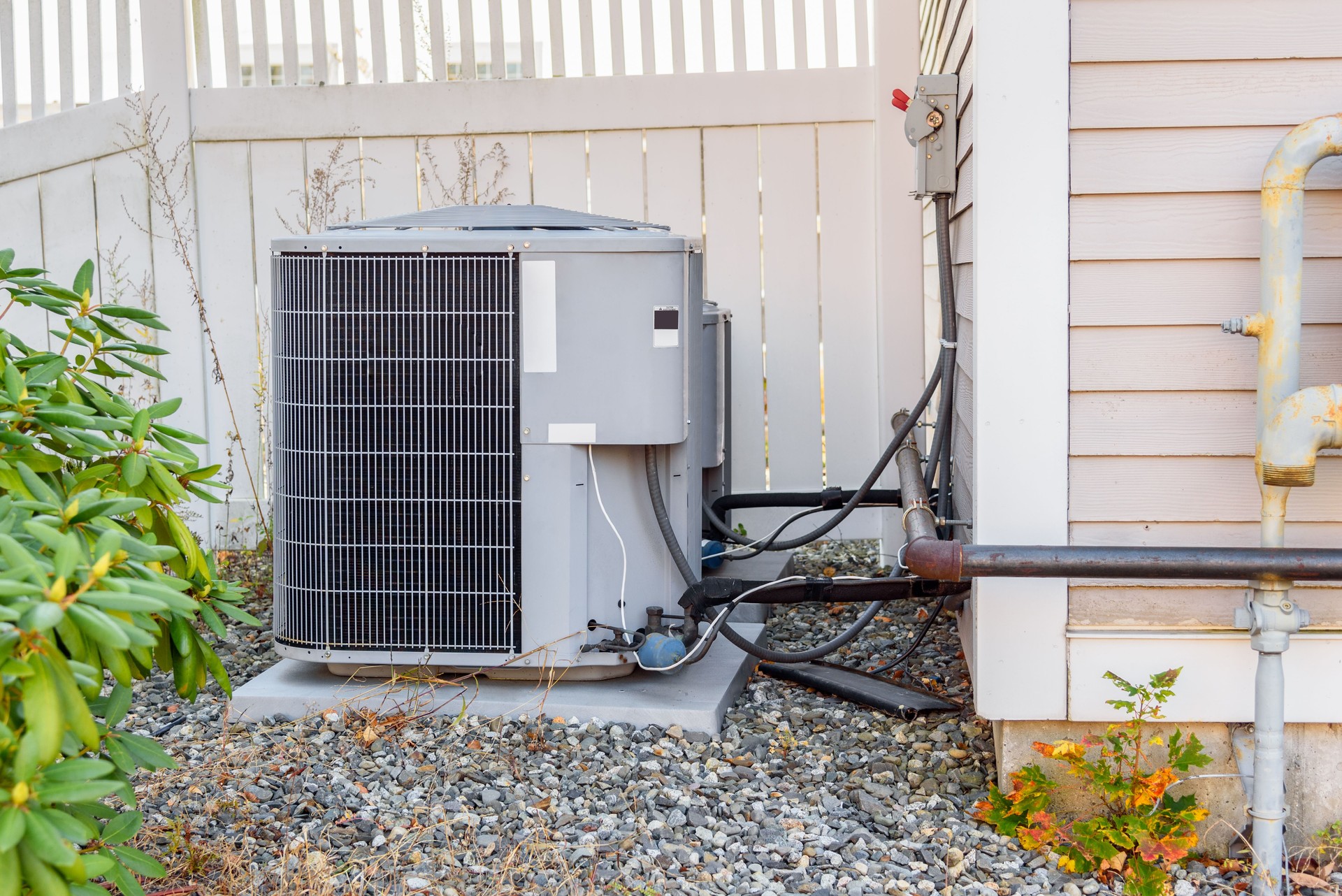 Air conditioning outdoor unit by a fence in a house backyard